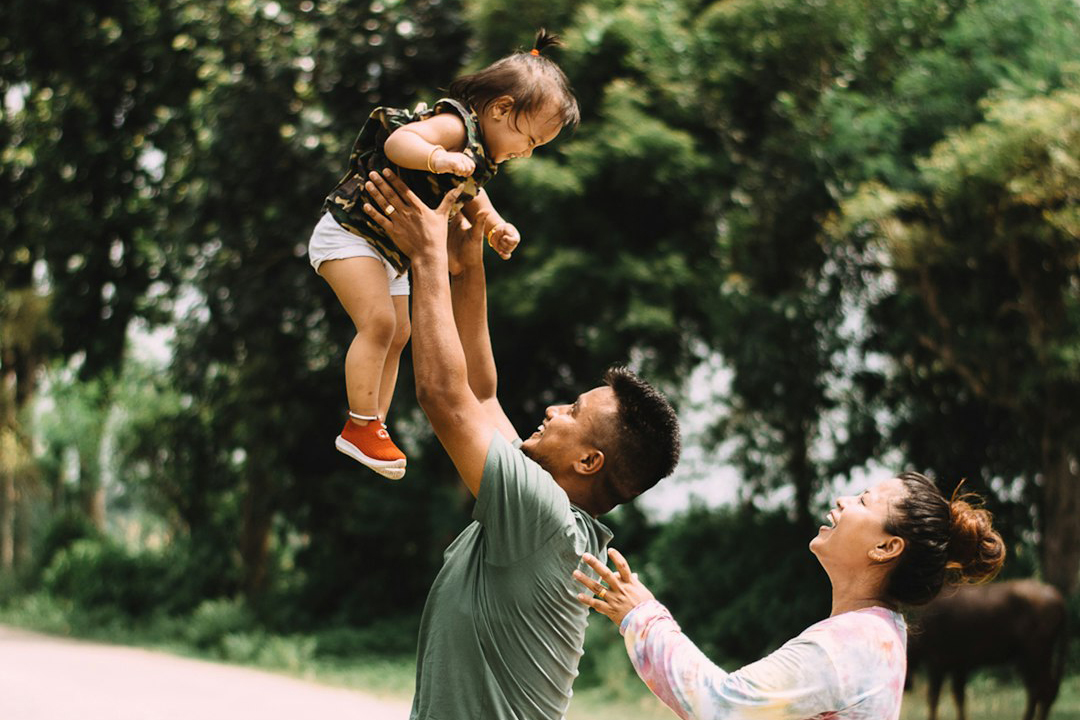 A happy family with a baby, smiling and playing together in a bright, sunlit room.